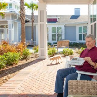 A senior citizen enjoying a relaxing day outdoors, reading a newspaper while their pet dog strolls nearby.
