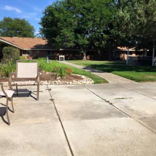 A sunny backyard scene featuring a well-maintained lawn and patio with chairs.