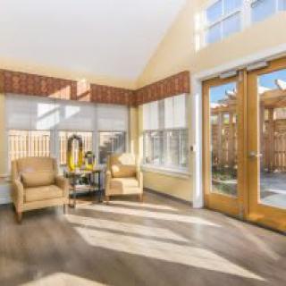 A bright and cozy sunroom featuring two armchairs, wooden flooring, and large glass doors letting in natural light.