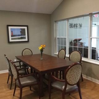 A conference room featuring a wooden table, six chairs, and a vase of flowers on the table, with a window and artwork on the wall.