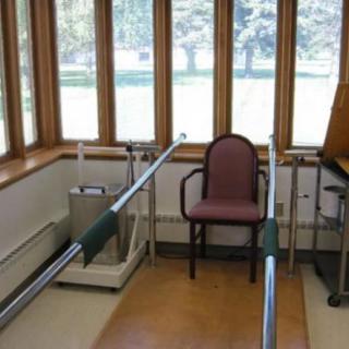 A physical therapy room with parallel bars and a chair for rehabilitation exercises.
