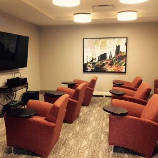 A cozy lounge area with orange chairs facing a large television.