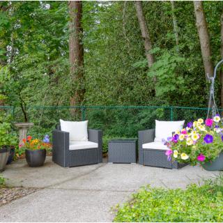 A cozy patio setup with two chairs and vibrant flower arrangements surrounded by lush greenery.