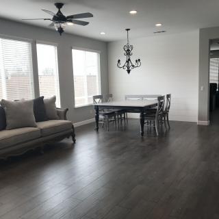 A spacious living and dining area featuring hardwood floors, ample windows, a ceiling fan, and a chandelier.