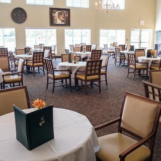 A spacious dining area with neatly arranged tables and chairs, decorated with flowers.