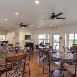 A spacious indoor dining area with multiple tables and chairs, ceiling fans, and large windows.