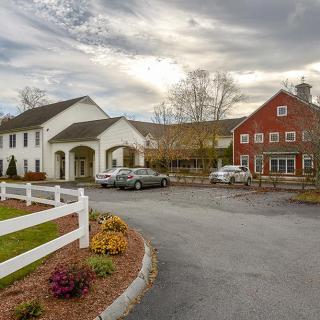 A scenic view of a white building and red barn with a parking area in front.