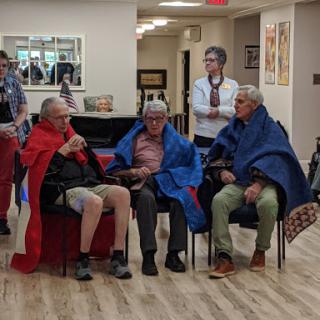 A group of elderly individuals wrapped in colorful blankets, seated comfortably in a communal space.