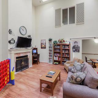 A cozy living room with a high ceiling, featuring a fireplace, television, bookshelf, and comfortable seating.