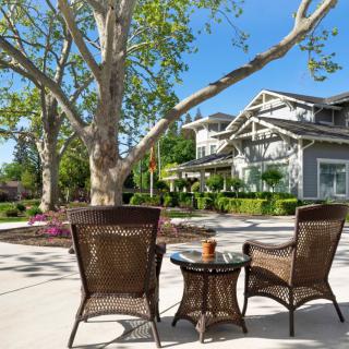 A tranquil patio with wicker chairs and a table overlooking a garden and house on a sunny day.