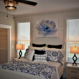A cozy bedroom with elegant decor, featuring a bed with patterned bedding and pillows, two bedside lamps, and a large floral painting above the headboard.