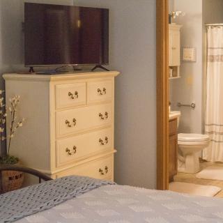 A cozy bedroom with a dresser and TV, leading into an adjoining bathroom.