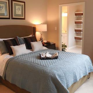 A cozy bedroom featuring a neatly made bed with multiple pillows, bedside lamp, and decorative artwork on the walls.