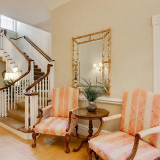 A cozy hallway with elegant chairs, a wooden table, and a decorative mirror beside a staircase.
