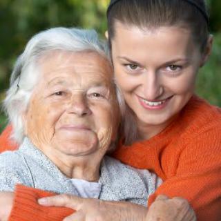 A young woman embraces an elderly woman, both smiling warmly outdoors.