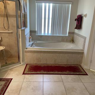 A bathroom with a shower, bathtub, and red rugs on a tile floor.
