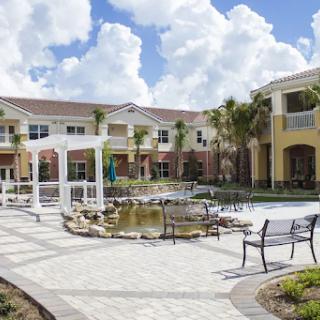 A beautiful courtyard featuring a serene water pond and comfortable benches, surrounded by residential buildings under a partly cloudy sky.