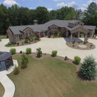 Aerial view of a large mansion with a circular driveway and landscaped surroundings.