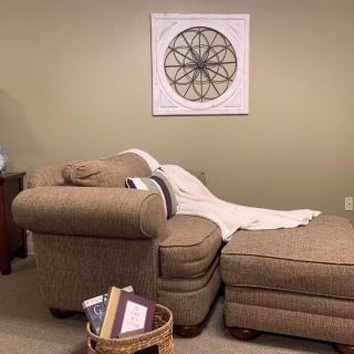 A cozy living room corner with a comfortable chair, matching ottoman, and a basket of books.