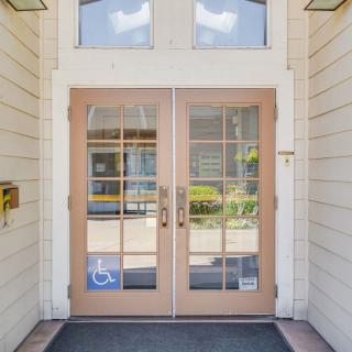 Glass double doors serving as the entrance to a building, featuring accessibility signage.
