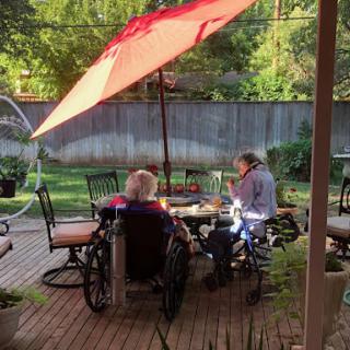 Two elderly individuals enjoying time together on a patio under a sunshade.