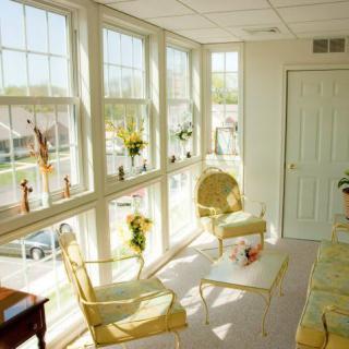 A bright sunroom featuring large windows, elegant chairs, and a small table adorned with decorative items.