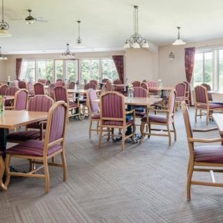 An empty dining room with multiple tables and chairs, featuring large windows and curtains.