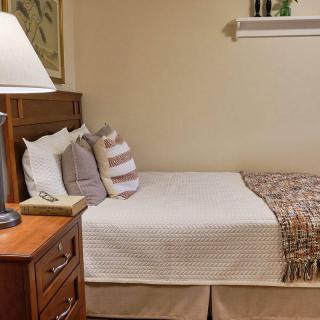 A cozy bedroom features a neatly made bed with pillows and a quilt, accompanied by a wooden nightstand with a lamp.