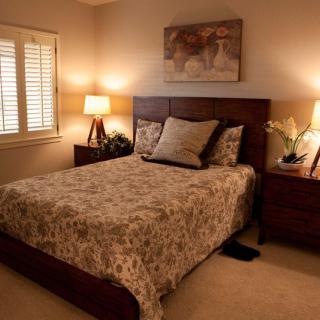 A cozy bedroom with warm lighting, featuring a bed with patterned bedding, two lamps on nightstands, and artwork above the headboard.