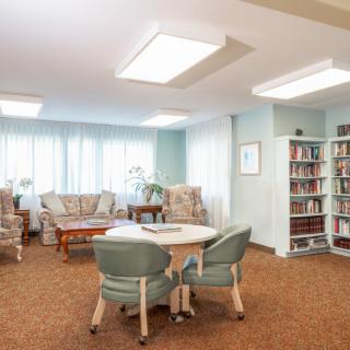 A cozy living room with a small library, featuring comfortable seating, a central table, and bookshelves.