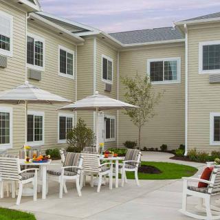 A cozy courtyard with outdoor seating and umbrellas, surrounded by a two-story building.
