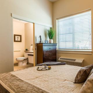 A cozy bedroom with a large window, featuring warm decor and an adjacent bathroom.