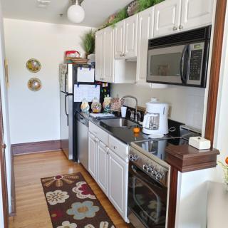 A compact kitchen with white cabinets, featuring a microwave, stove, and refrigerator.