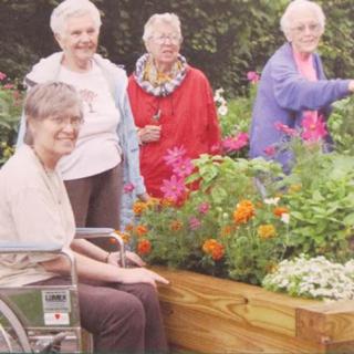 A group of elderly women enjoying a day in the garden, surrounded by colorful flowers.
