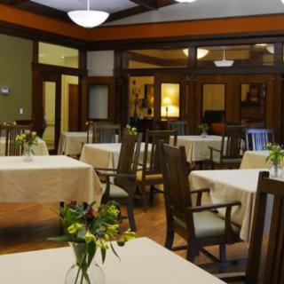A cozy dining room with neatly arranged tables and chairs, adorned with small floral centerpieces.