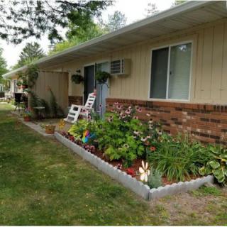 A garden with colorful flowers in front of a brick house, featuring a white rocking chair on the porch.