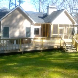 A cozy house with a wooden deck and a grassy yard on a sunny day.