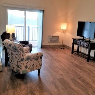 A cozy living room with chairs, lamps, a TV, and wood flooring.