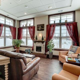 A cozy living room with large windows, elegant curtains, a fireplace, and comfortable seating.
