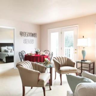A cozy living room with elegant furnishings, featuring plush chairs, a table set for dining, and a soft lamp lighting the space.