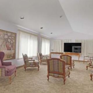 A spacious living room with several chairs arranged around a television and large windows with curtains.