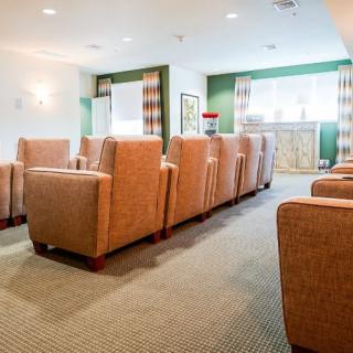 A well-lit room with multiple cushioned chairs arranged in rows, featuring a cozy carpet and windows allowing natural light.