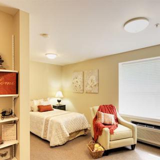 A cozy bedroom with soft lighting, featuring a neatly made bed, an armchair draped with a blanket, and tasteful decor.