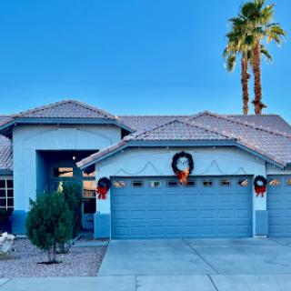 A beautifully decorated home with holiday wreaths on the garage doors, surrounded by palm trees under a clear blue sky.