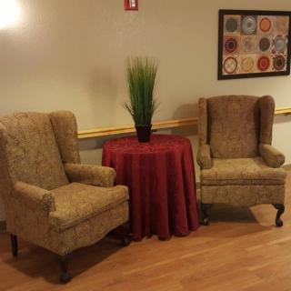 A cozy seating area with two armchairs, a small table covered with a red cloth, and a potted plant.