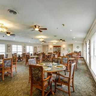 An inviting dining room with multiple tables and chairs, featuring ceiling fans and natural lighting from large windows.