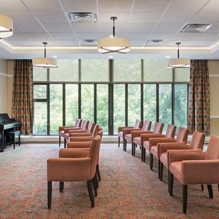 A well-lit conference room with rows of chairs facing a piano, large windows, and stylish ceiling lights.