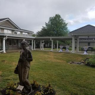 A statue stands on a lawn amidst two buildings under an overcast sky.