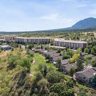 Aerial view of a residential area with buildings, surrounded by lush greenery and mountains in the background.