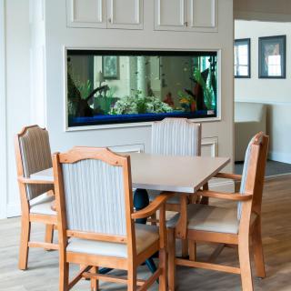 A cozy dining area featuring a wooden table and chairs, complemented by a built-in aquarium in the wall.